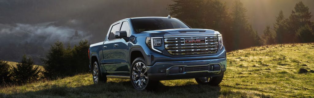 A GMC Sierra parked on a scenic grassy hillside with mountains in the background.