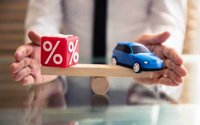 A blue toy car and red percent sign cube on wood which holds by an person